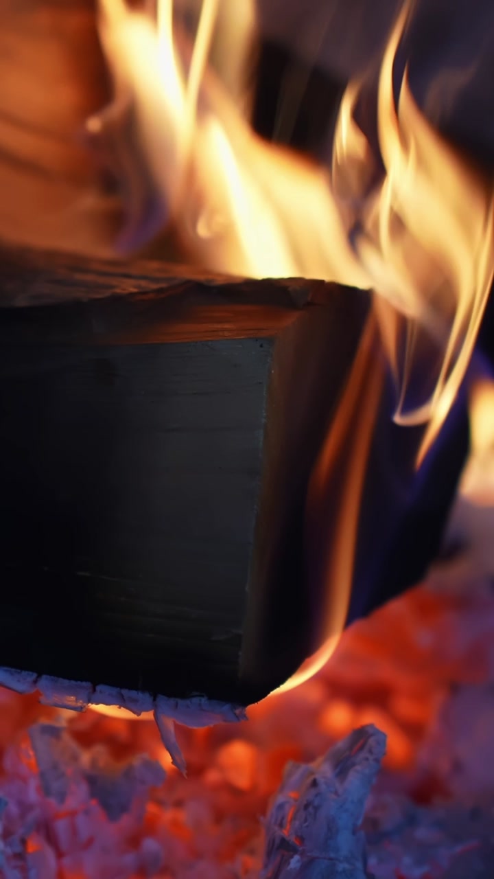 Vertical close-up of flames and smoke behind fireplace glass on a wood stove, creating a cozy winter home mood with warm glow and soot-stained door.