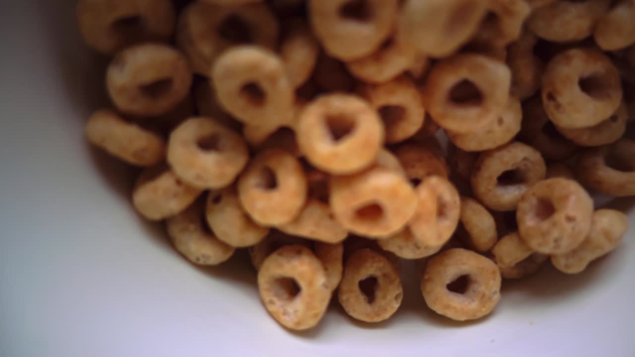 Top-down slow motion shot of cereal pieces falling through the air into a bowl, captured with shallow depth of field, creating a floating, suspended effect as the cereal descends toward the bowl