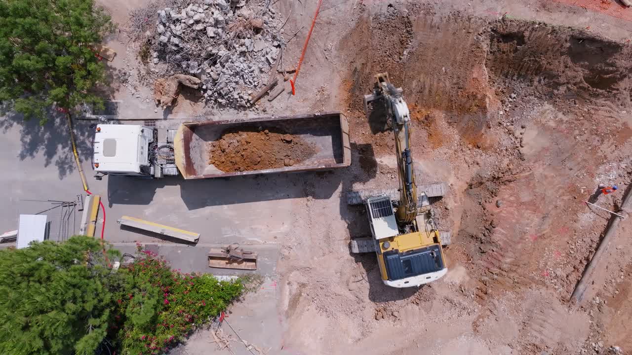 vista aérea de arriba hacia abajo de la excavadora recolectando arena y poniéndola en el camión en un sitio de construcción