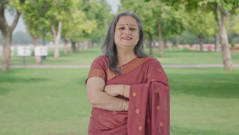 happy indian old woman standing crossed hands in park