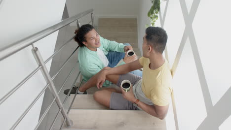 feliz pareja de hombres homosexuales diversos sentados en la escalera soleada tomando café y hablando, en cámara lenta