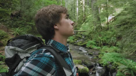 white male hiking through peaceful lush green forest with waterfall in background  zooming from wide to close up of face