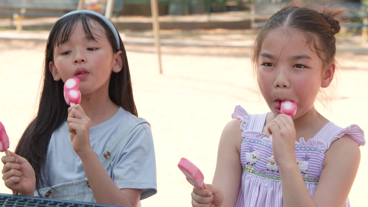 夏の晴れた公園で、2人の少女が屋外でピンクの蝶型アイスキャンディーを楽しんでいる。