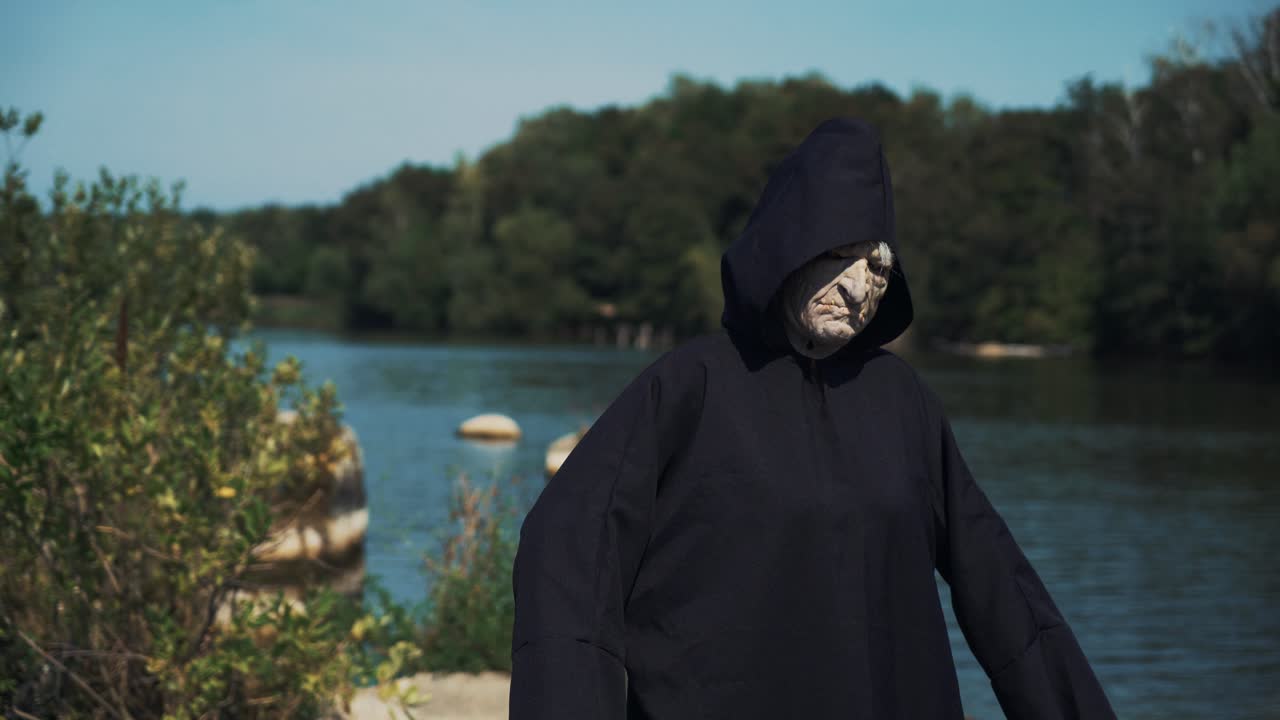 Eerie witch on river bank watches the camera. Halloween costume.