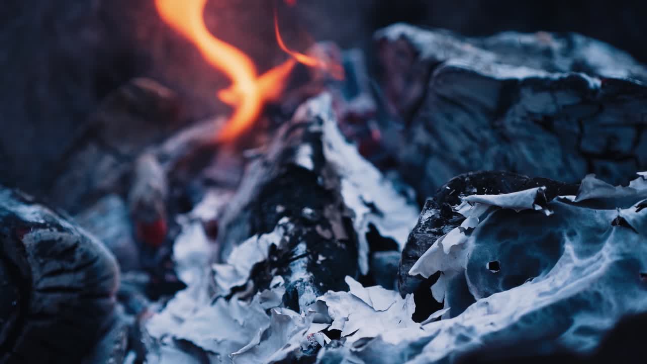 Close-up burning fire with ash. Paper burns on smoldered logs. Smoldering burning logs in fire with ash and coals. Slow motion.