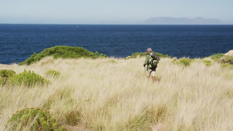 african american man hiking with hiking poles in countryside by the coast