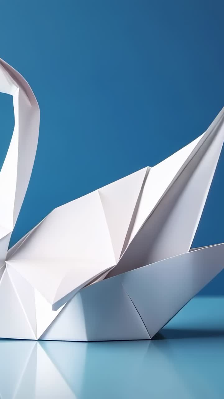 Vertical video: Panning camera revealing white origami swan on glass table, with blue backdrop