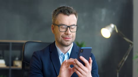 Businessman-In-Glasses-Using-Smartphone-In-The-Office