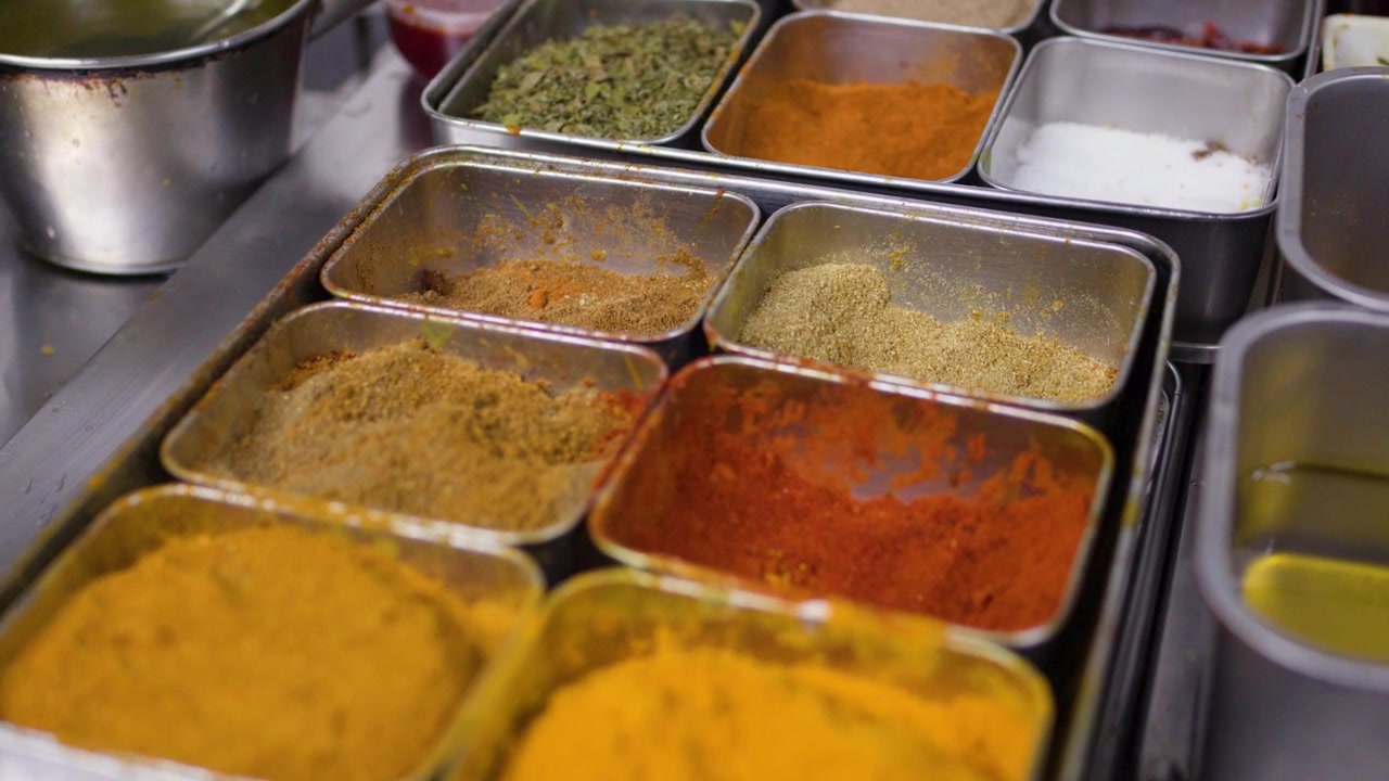 Varie spezie secche colorate disposte in contenitori per la preparazione in acciaio inossidabile all'interno di una cucina di un ristorante