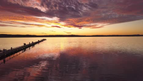 extraordinaria puesta de sol de fuego dorado con nubes reflexionando sobre el agua y la gente en la silueta