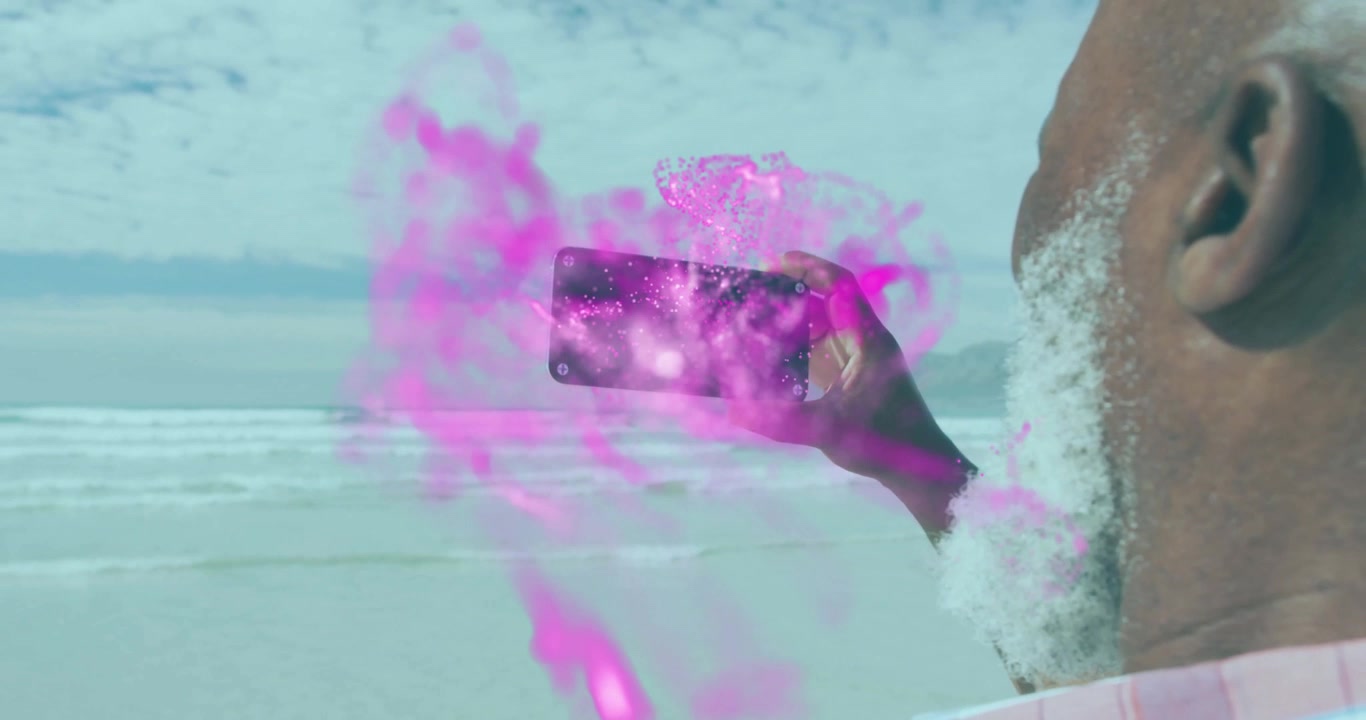 Hombre maduro sosteniendo un smartphone en la playa, proyectando partículas magenta-rosa sobre el océano para una demostración tecnológica