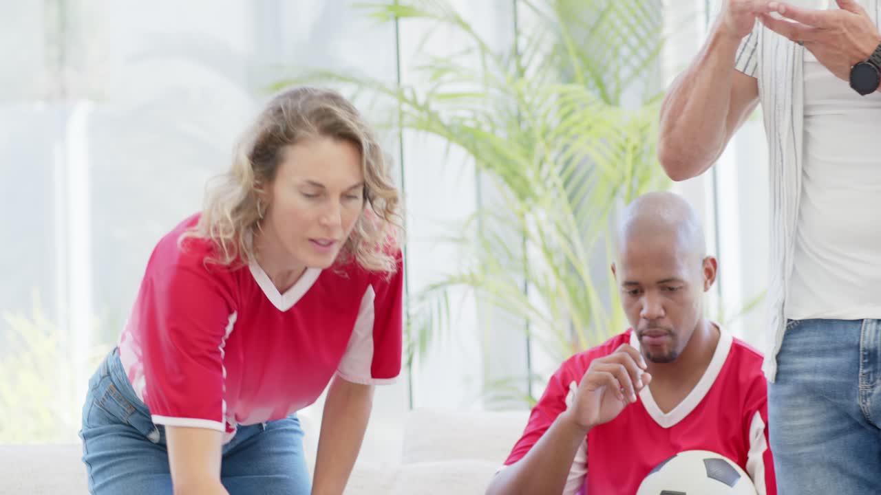 Diverse Freunde platzieren Getränke für das Spiel zu Hause, sitzen und suchen Snacks neben einem Fußball aus.