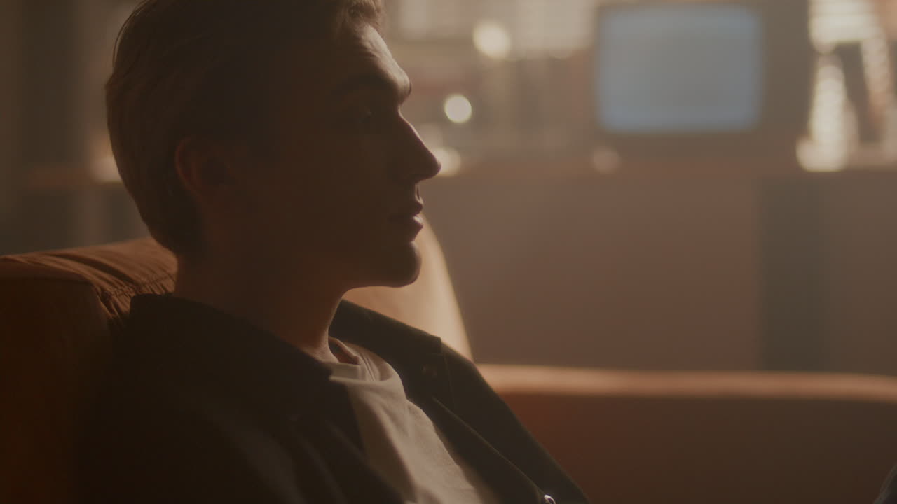 Young Man Sitting on Couch in Living Room, Looking Thoughtfully Ahead