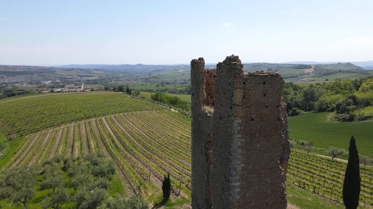 Ripresa aerea grandangolare con drone che orbita attorno a un antico castello circondato da una vista panoramica di vigneti e montagne all'orizzonte situato nella campagna abruzzese in Italia