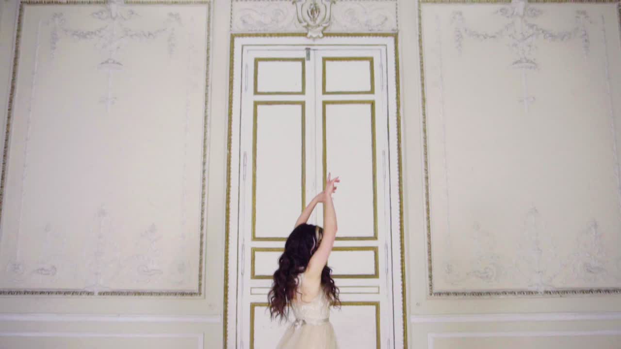 긴 이브닝 드레스를 입은 젊은 여성이 문 근처 홀에서 춤을 춘다