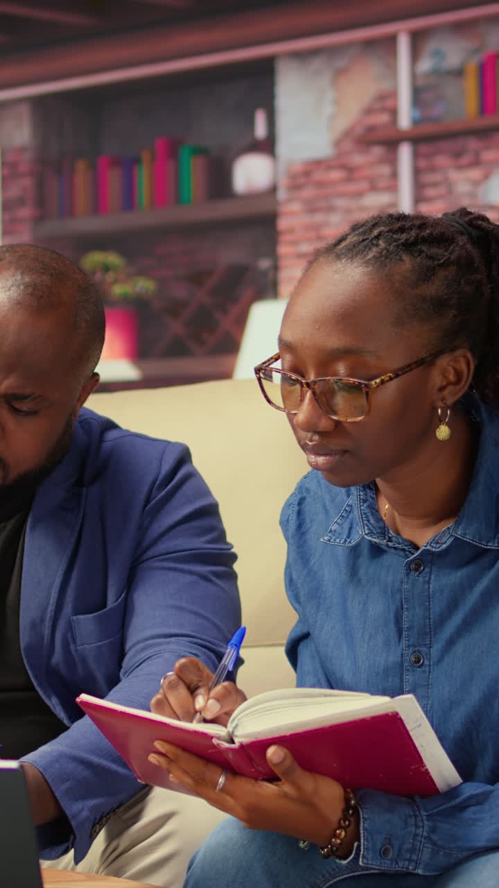 African American Woman Writing in Notebook while Collaborating with Man
