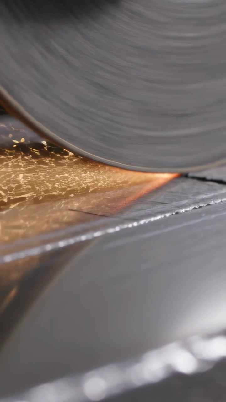 Video vertical: Rueda abrasiva gruesa en contacto con una pieza de metal en un banco de trabajo para cortar metal, produciendo chispas.