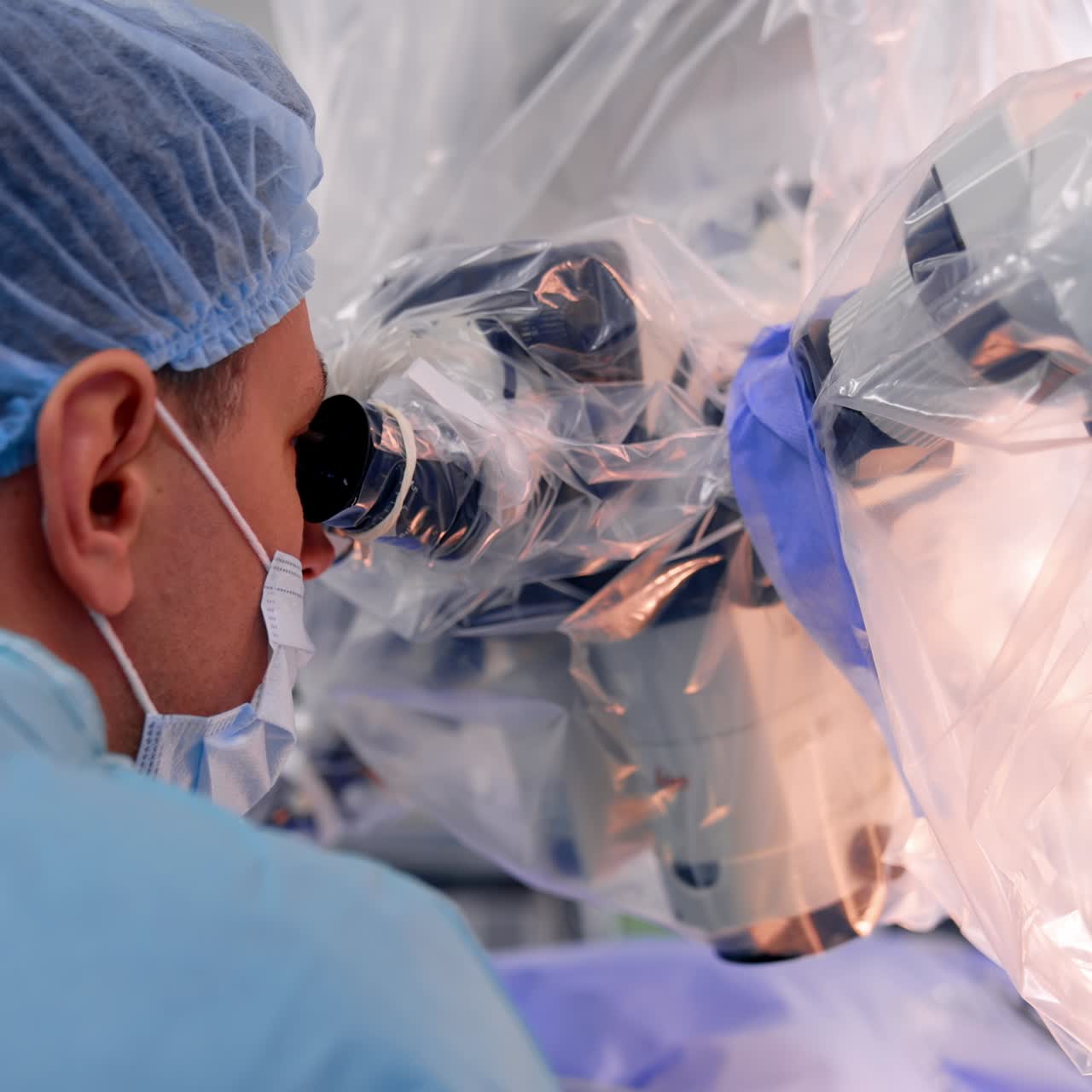 Vista posteriore di un medico con mascherina e cuffia che guarda nel microscopio. Neurochirurghi al lavoro. Primo piano.