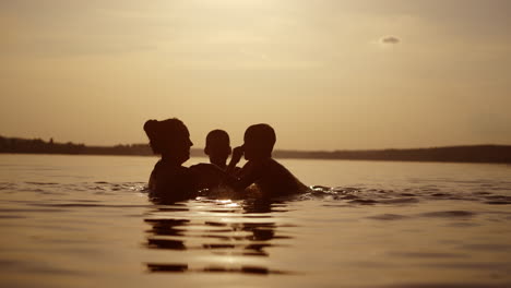 woman and two boys in water at sunset. mother throws her sons up into water in the evening. children having great time with their mother in the lake at summertime.