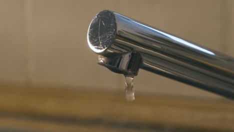 una gota de agua cae del grifo del fregadero en cámara lenta, cerca del grifo