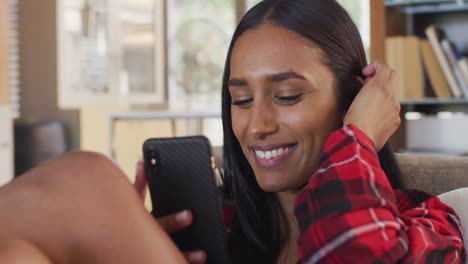 Mixed-race-woman-using-smartphone,-having-a-video-conversation-sitting-on-couch