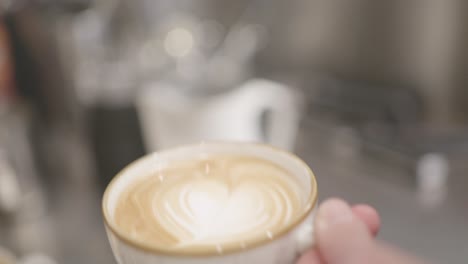 Barista-Vertiendo-Lentamente-Una-Taza-De-Leche-En-Una-Taza-De-Café-Capuchino-Y-Formando-Un-Corazón-Blanco-Cremoso-En-La-Superficie-Del-Café