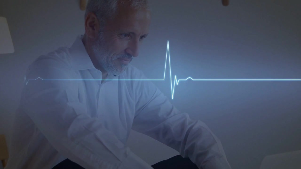 Uomo anziano appoggiato, che si protende su una poltrona del soggiorno, mentre un picco ECG viene monitorato tramite laptop per il controllo cardiaco