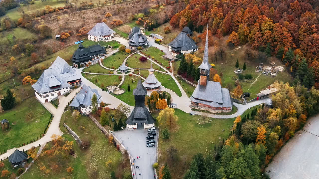 Aerial drone view of the Barsana Monastery, Romania. Main church and other buildings, visitors, hills covered with yellowing forest around