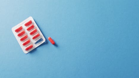 video of red pills in blister pack and one out, on blue background with copy space