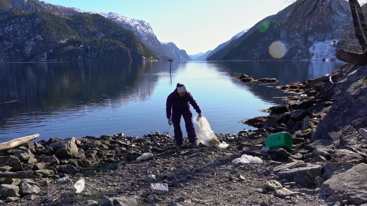 Kvinde samler plastikaffald op fra en klippestrand i Norge, viser det til kameraet