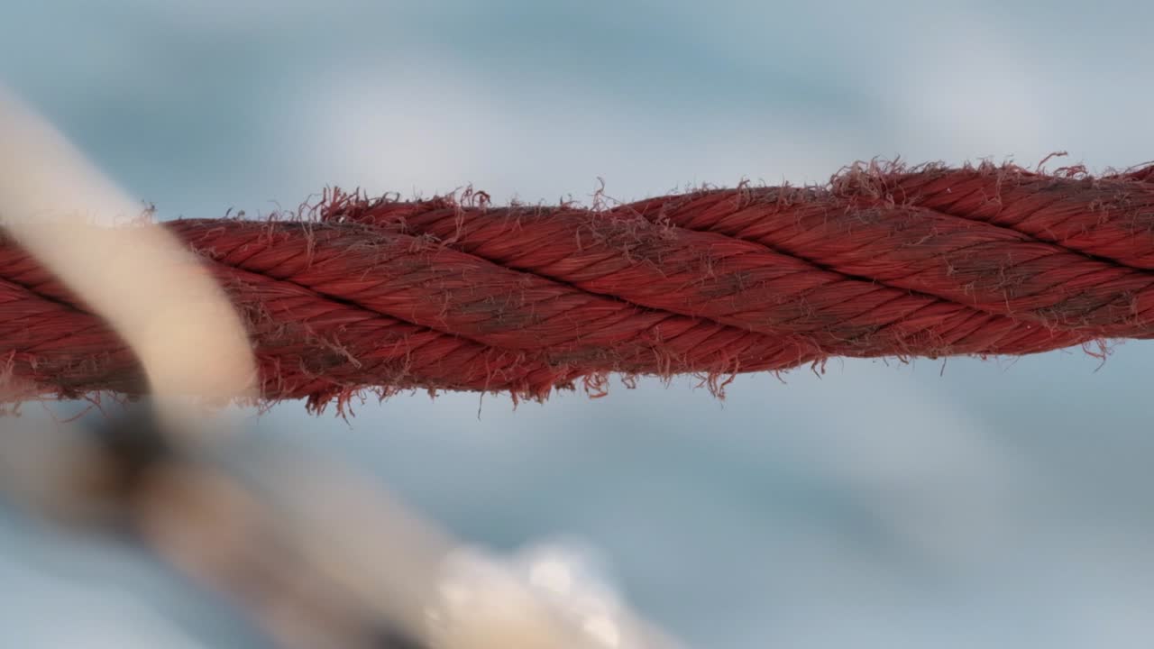 cuerda roja de un velero con olas de mar salpicando en segundo plano.
