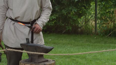 a revolutionary war reinacter blacksmith hammers out a hot piece of molten metal out on an anvil