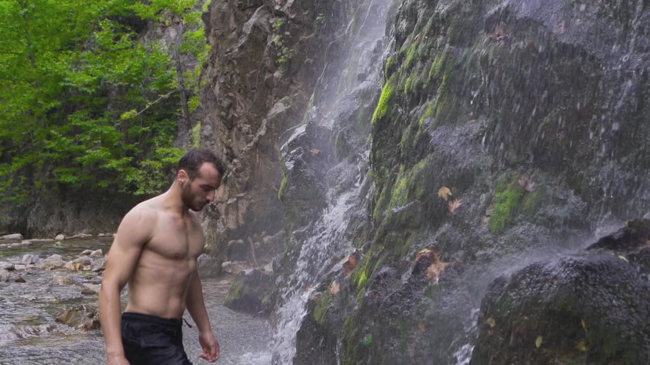un hombre deportivo se moja el cabello frente a una cascada.