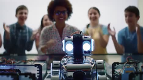 Excited students cheer and applaud during an engaging robotics demonstration in a classroom. A shiny robot takes center stage as their anticipation fills the room.