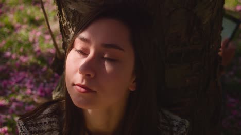 Young-Girl-Sitting-Under-The-Tree-With-Sunlight-On-Her-Face