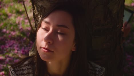 joven sentada bajo el árbol con la luz del sol en su cara