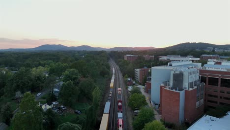 static aerial of riding train in american suburb district with green trees at golden sunset. campus building and noble housing area with house and homes. panorama shot.