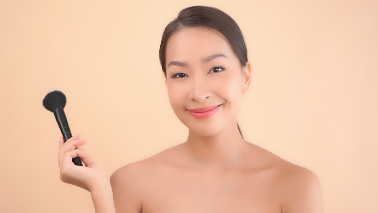 Close up of beautiful Asian woman's face blending her makeup with a brush