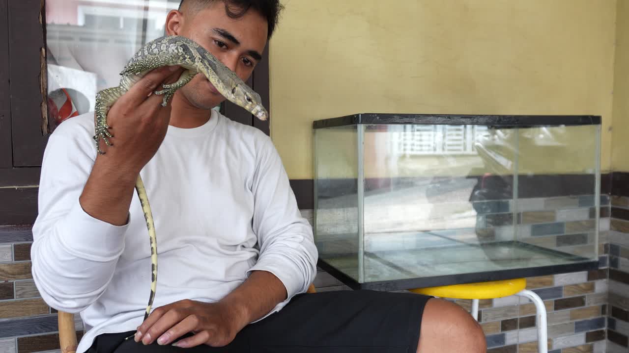 Uomo asiatico che tiene in mano e gioca con una lucertola varano
