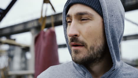 close-up view of the sweaty face of the male boxer in grey hoodie during a training outdoors an abandoned factory on a cloudy morning