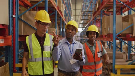 diverse male and female workers wearing safety suits and talking in warehouse