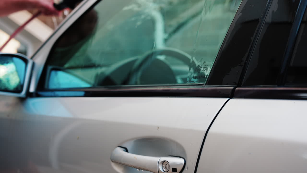 Chisinau, Moldova - August 18, 2025: A man washing a silver car window with a cleaning brush, removing soap and dirt