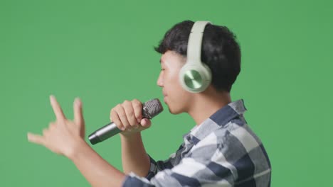 close up side view of young asian teen boy holding a microphone and rapping on the the green screen background