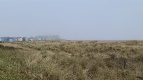 cabañas de playa en una costa invernal brumosa y dunas de arena cubiertas de hierba bajo un cielo gris neblinoso