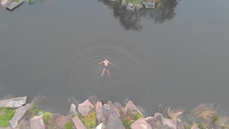 Una-Toma-Aérea-A-Vista-De-Pájaro-De-Un-Hombre-Nadando-En-Agua-Fría-En-Una-Presa-Agrícola-En-Invierno