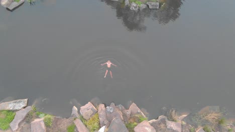 una toma aérea a vista de pájaro de un hombre nadando en agua fría en una presa agrícola en invierno