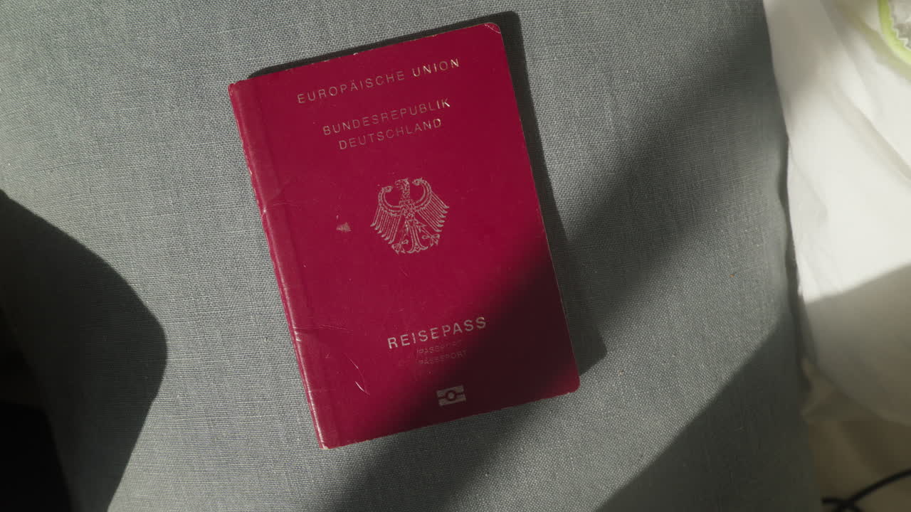 A German passport (Reisepass) lies on a light-colored surface. The passport cover is red with gold text and the German coat of arms emblem. Image showcases travel document of the Germany.