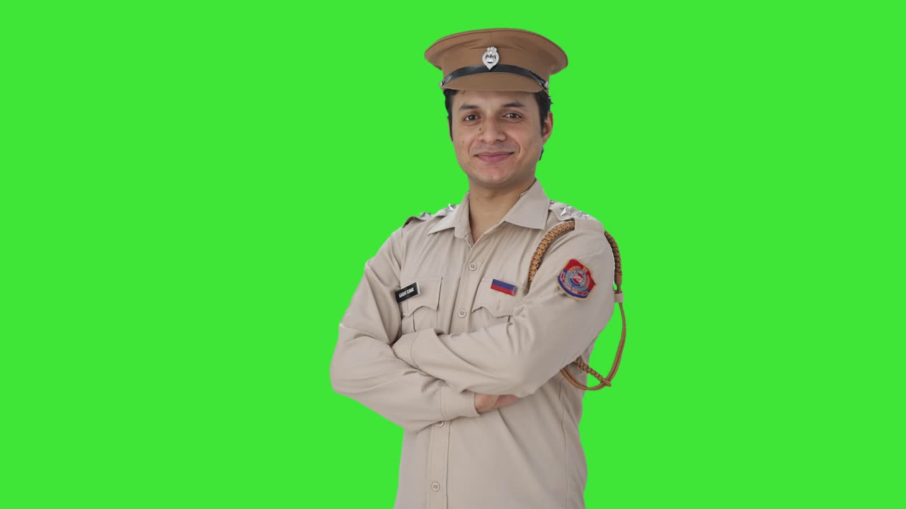 Ritratto di felice poliziotta indiana in piedi con le braccia incrociate Green screen