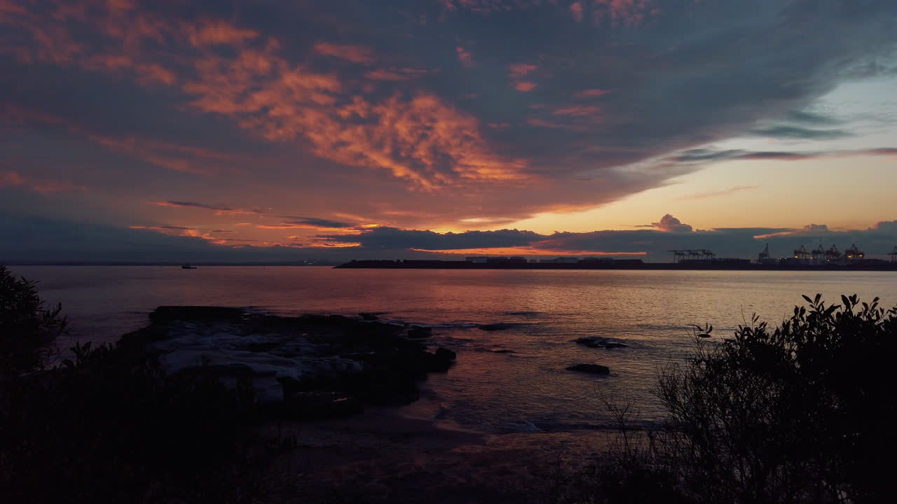 Clouds in sky lit up by final sunlight creating spectacular colors over bay