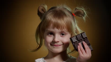 retrato en primer plano de un niño adolescente con una barra de chocolate con leche mostrando el pulgar hacia arriba en un fondo oscuro